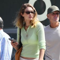 Gigi Hadid wearing a light green polo sweater, cream sweatpants, and brown ruched loafers in NYC