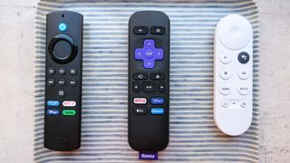 (L to R) The remotes for the Amazon Fire TV Stick lite, the Roku Express (2022) and the Chromecast with Google TV on a striped tray.
