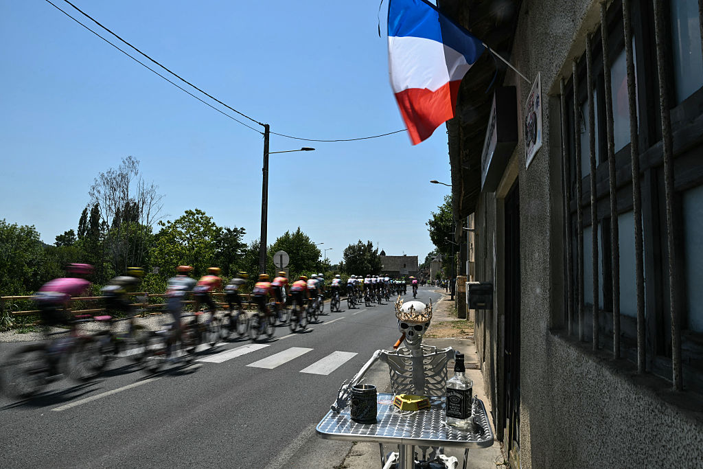 The pack of riders (peloton) cycles past a skeleton mannequin set up along the race route during the 8th stage of the 113th edition of the Tour de France cycling race, 180,4 km between Perigueux and Bergerac in southwestern France, on July 11, 2026. (Photo by Jeff PACHOUD / AFP)