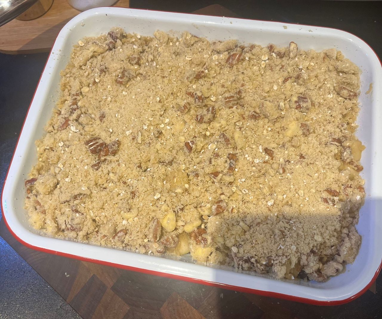 A white enamel dish with a red rim, with an unbaked crumble inside.