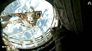 a spacewalking astronaut in a white spacesuit is seen through the open hatch of his spacecraft, with earth's cloudy skies behind him