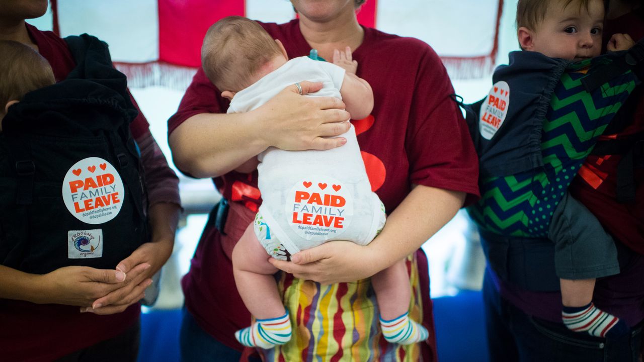 A woman holds a baby with a paid leave sticker on their bottom