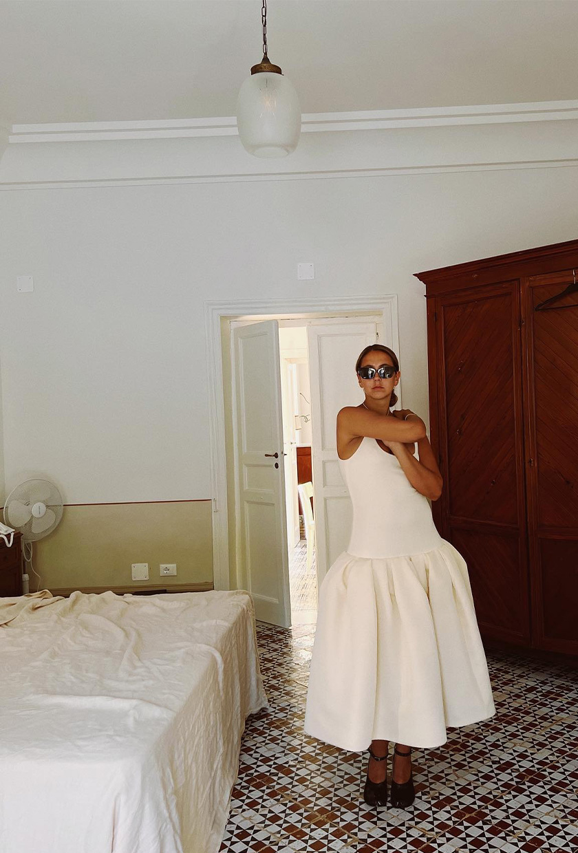 How to pack for Italy is shown in a picture of a woman wearing black sunglasses, a white dress, and black pumps