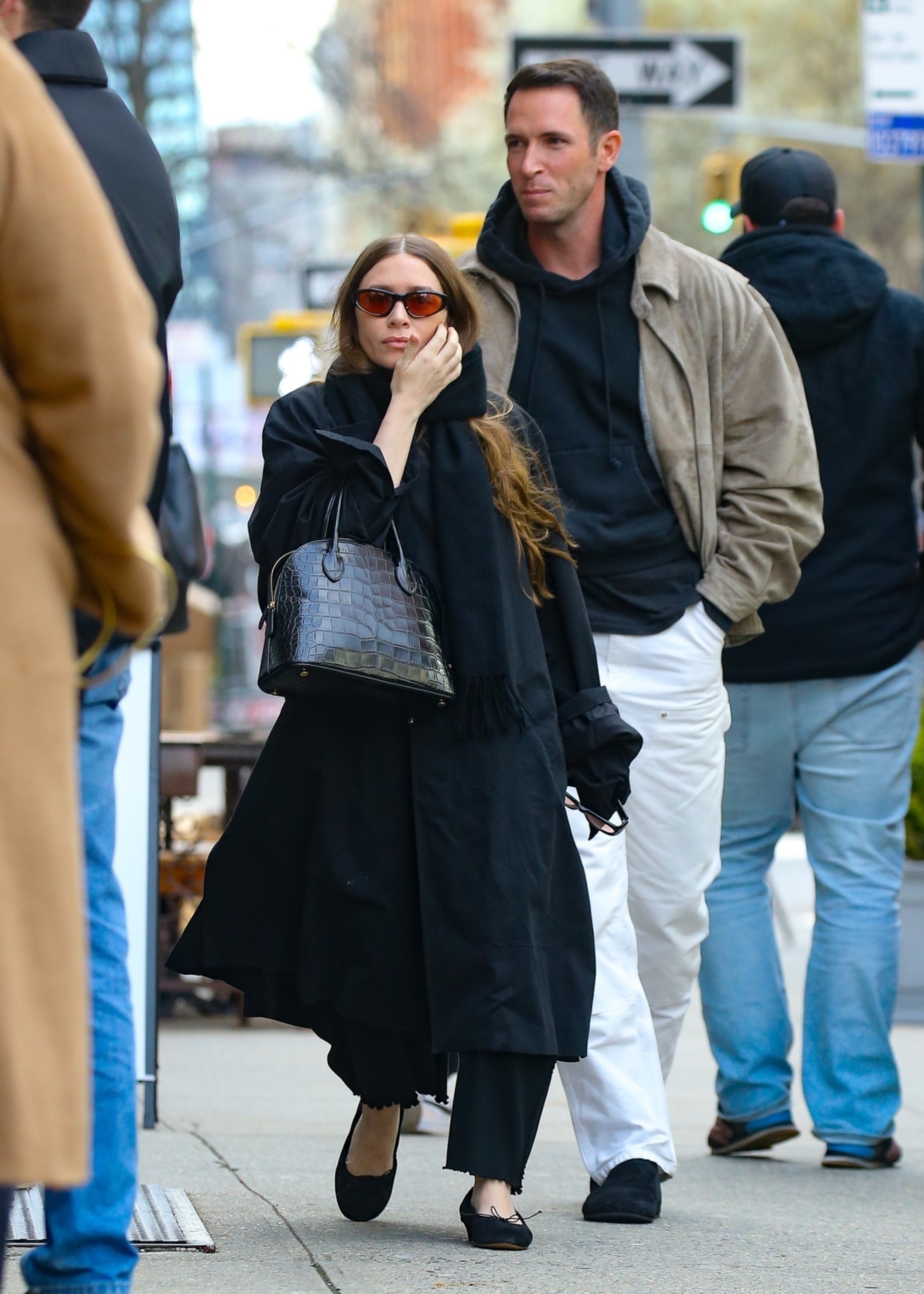 An image of Ashley Olsen wearing an oversized trench coat with black trousers, black ballet flats and a mock croc bag.