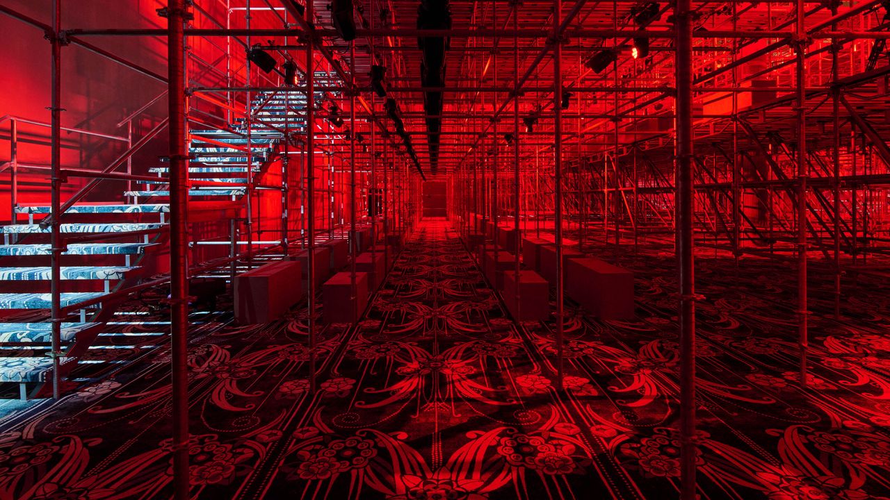 Prada A/W 2025 menswear runway show set featuring scaffolding and patterned carpet