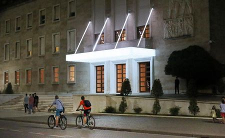 people riding bicycles in front of a stone building with a white entrance