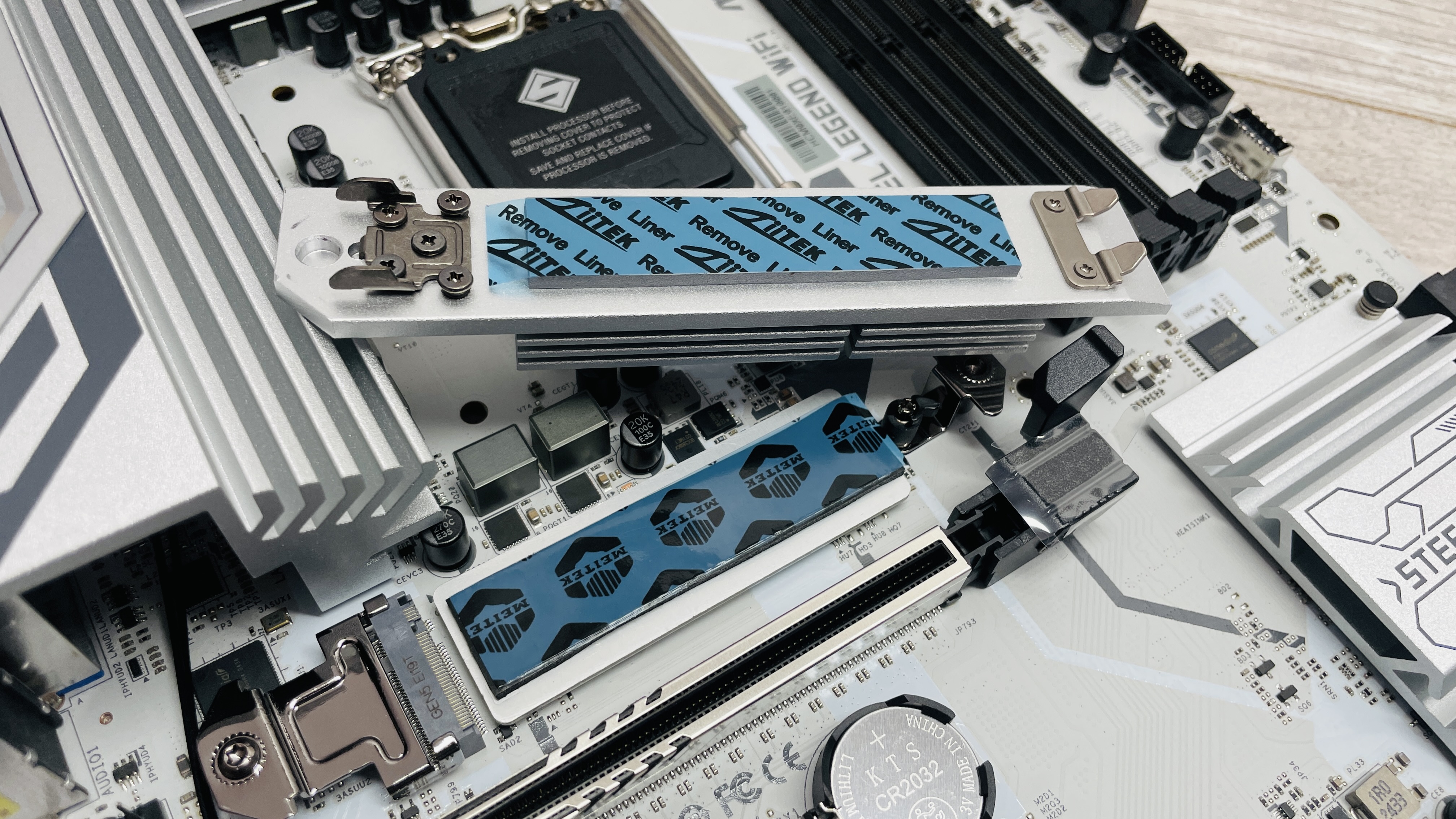 An ASRock B860 Steel Legend Wi-Fi motherboard on a desk with SSD covers removed.