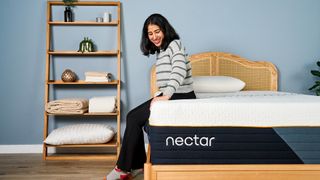 A woman sits on the side of the Nectar Ultra Hybrid Mattress in a bedroom, testing the edge support