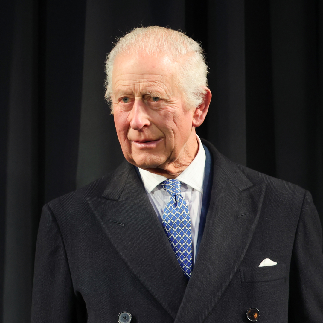 King Charles wears a dark overcoat with a white shirt and blue patterned tie
