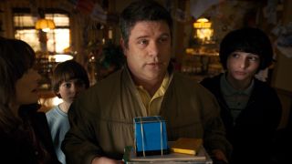 A press photo of Sean Astin as Bob in Stranger Things holding a blue box. 
