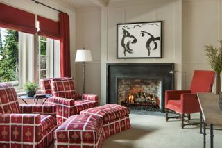 Red living room with fireplace, armchairs with red patterned upholstery and plain red upholstery, red blinds an curtains and neutral walls and floor