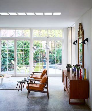 A mid-century modern living room with wooden furniture, orange chairs and large French windows.