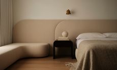 Beige wraparound upholstered headboard stretching from wall to wall and leading into a window bench