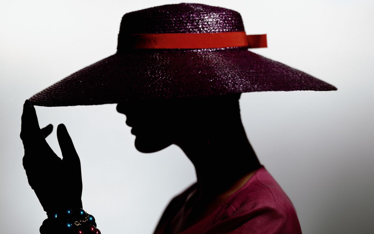 a model wearing a large red hat with wide brim casting a silhouette. 