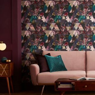 A living room designed with burgundy geometric and floral wallpaper with a pink velvet sofa