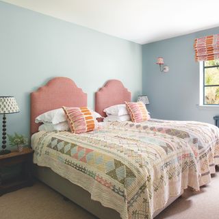 bedroom with blue walls and twin beds with pink upholstered headboards and patchwork quilts