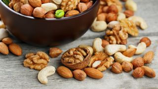 Bowl of mixed nuts with some nuts scattered onto the wooden table