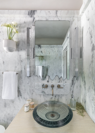 A marble bathroom with a mounted anthurium planter on the wall diagonally above the sink