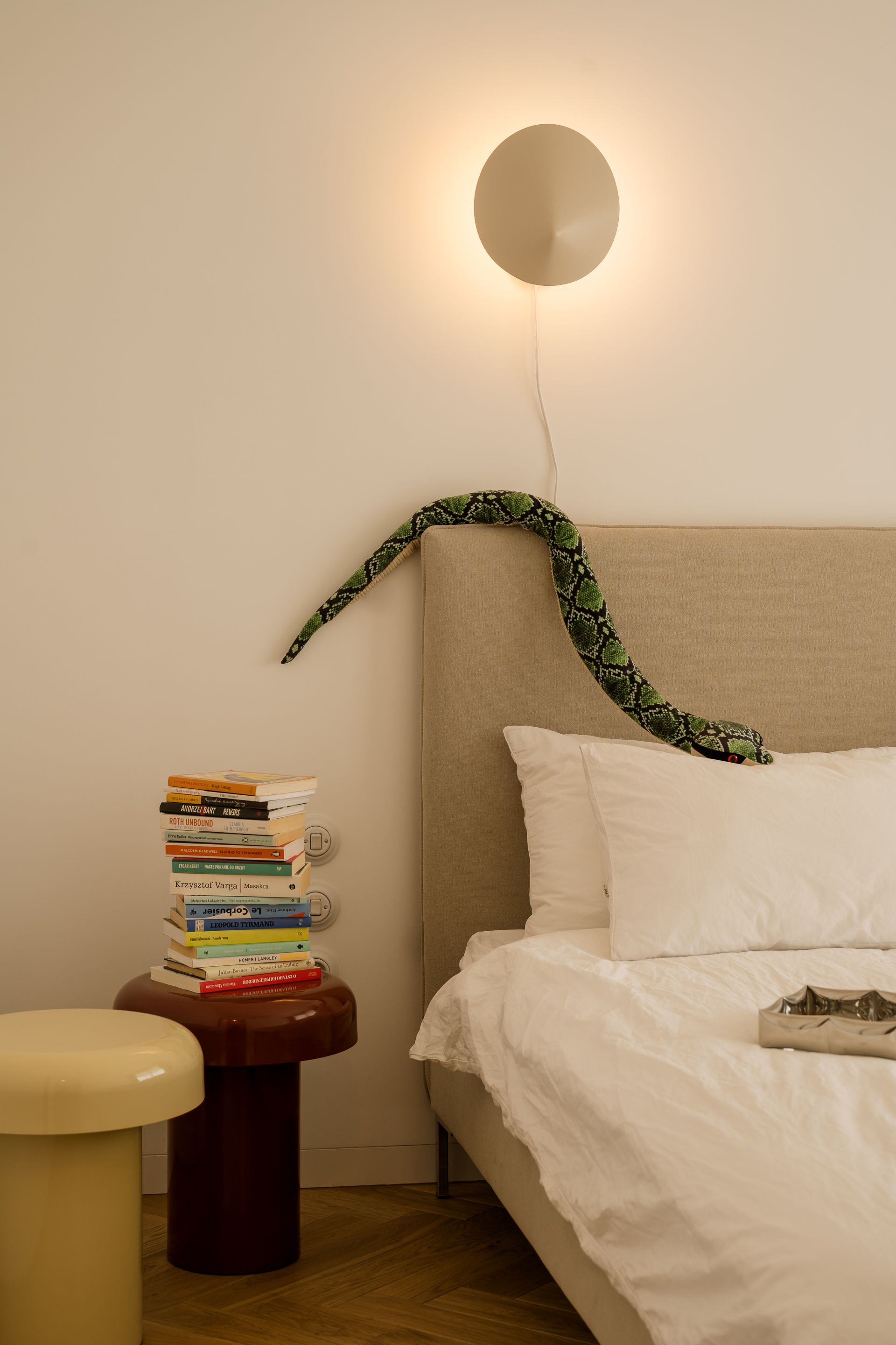 A plush snake climbs the headboard of a neutral bedroom