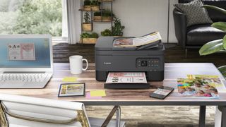 One of the best wireless printers, siting on a desk next to a laptop and other clutter
