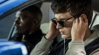 Baby (Ansel Elgort) wearing sunglasses and putting earphones in as Jamie Foxx sits next to him in the car.