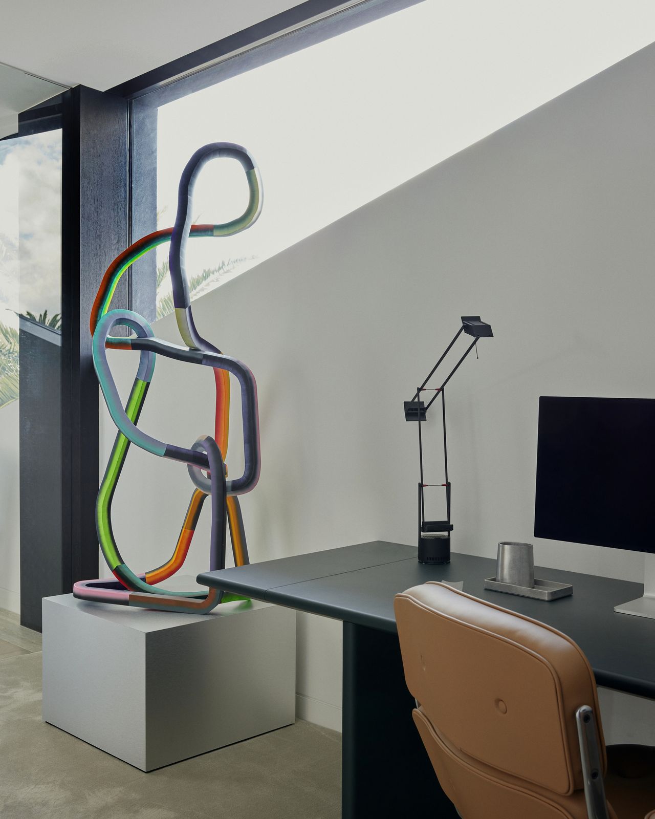 home office with tan office chair, table lamp, and large sculpture