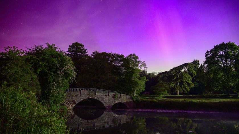 Vibrant Northern Lights over reflected in a still river with an old bridge
