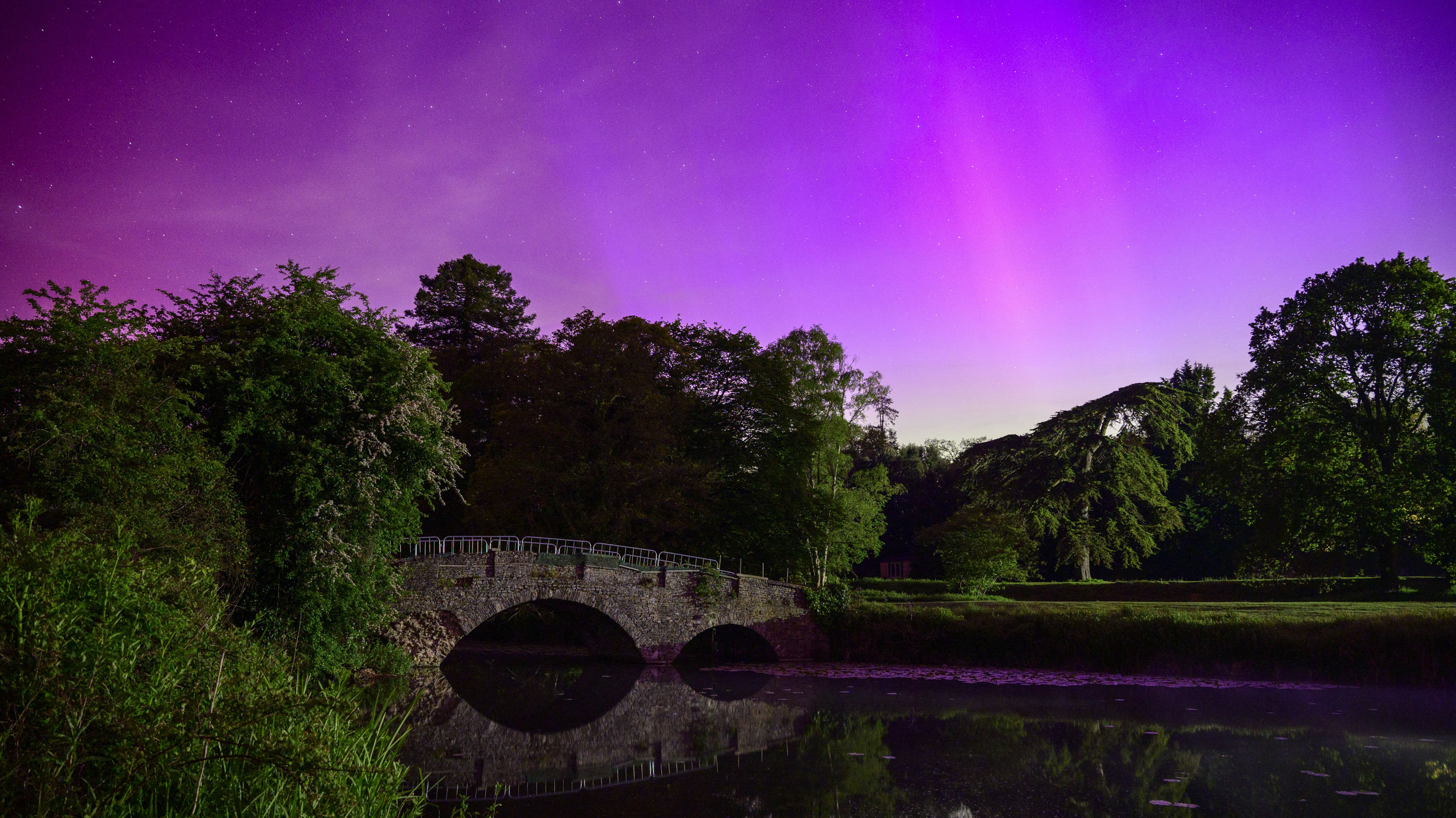 Vibrant Northern Lights over reflected in a still river with an old bridge