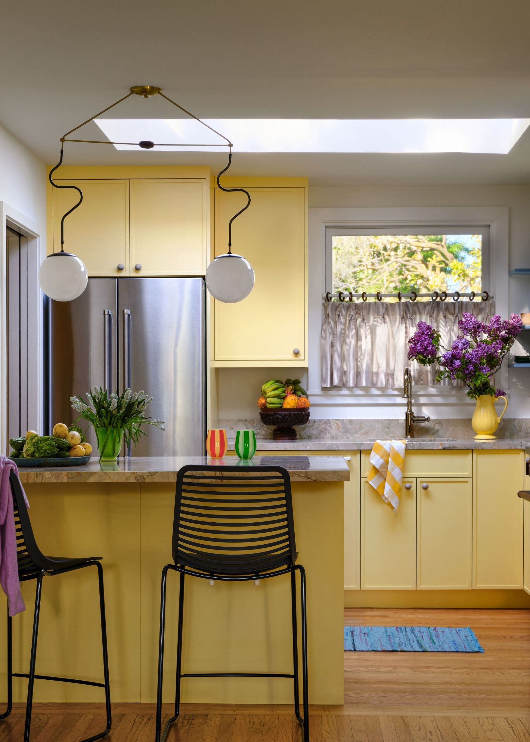 A kitchen with sunny yellow cabinets and island, tall bar stools and an organic countertop light 