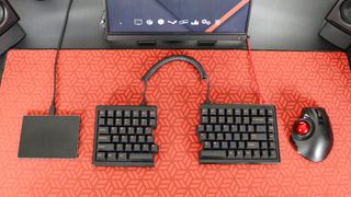 An overhead view of a trackpad, mechanical keyboard and a trackball mouse on a desk mat