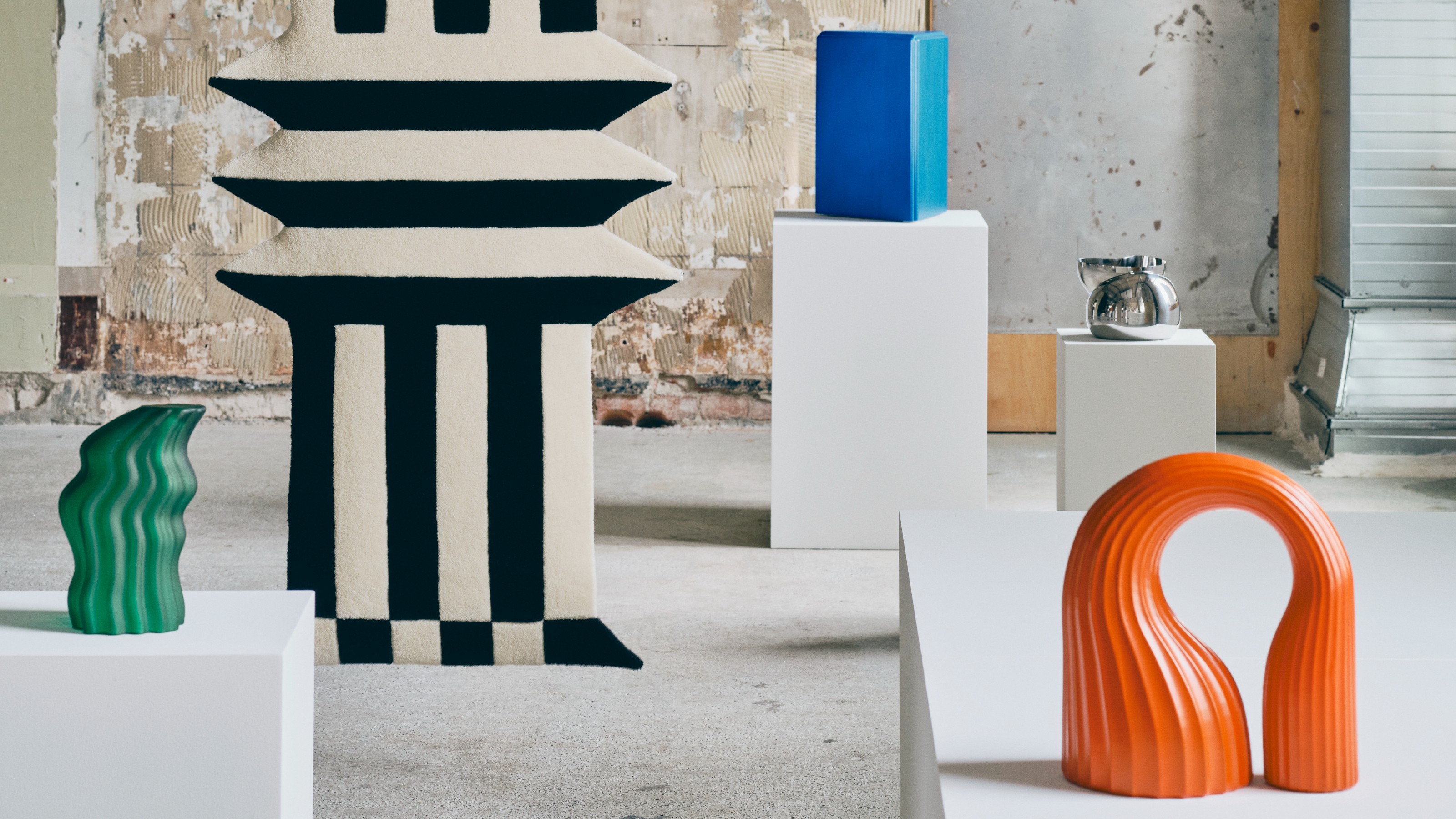 An industrial-style space filled with pillars displaying pieces from the IKEA KONSTRUNDA collection with a suspended black and white striped rug among them