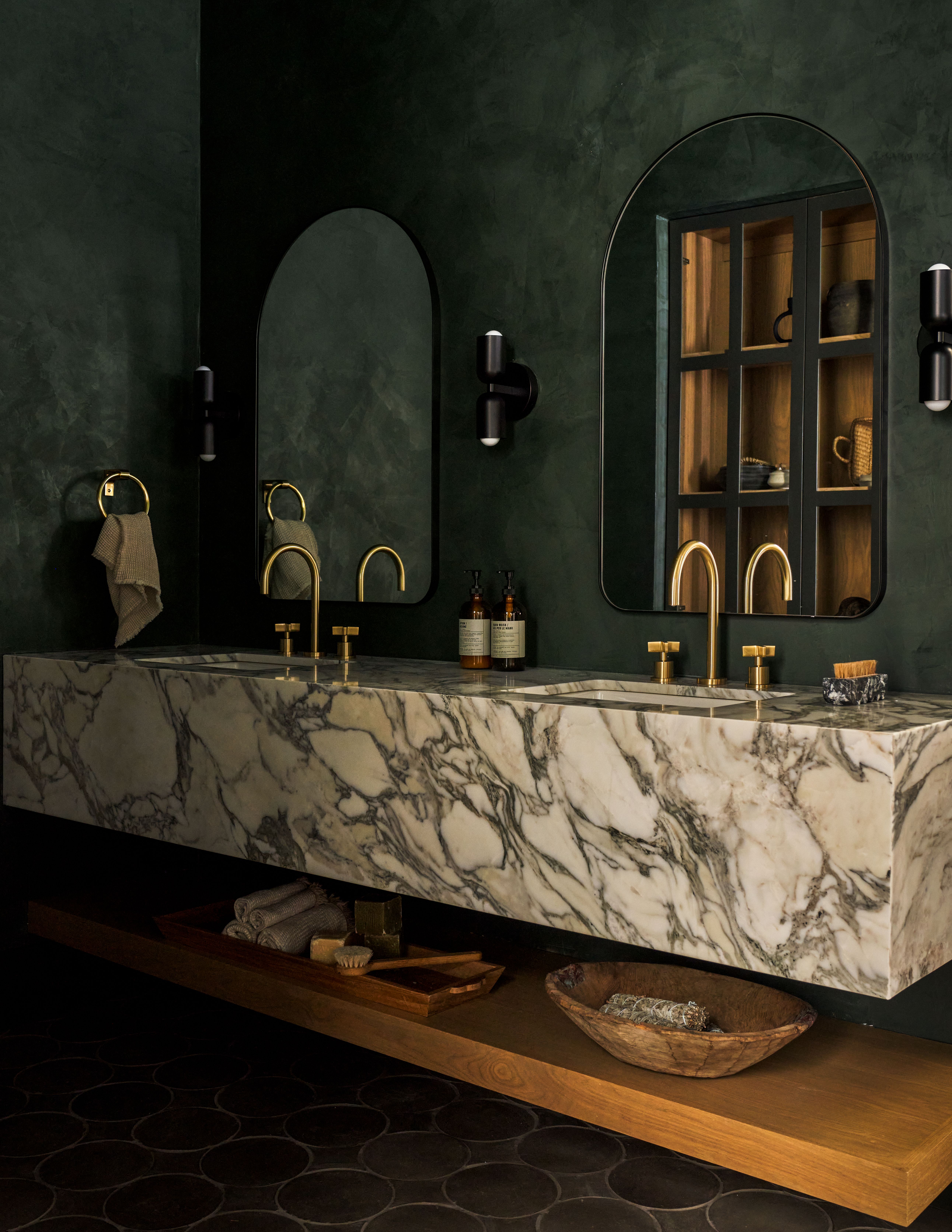 A bathroom painted in a deep forest green shade with a double marble vanity