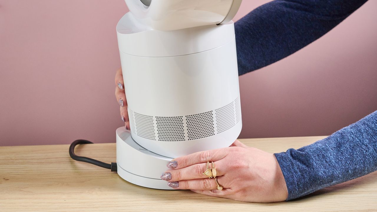 A woman is adjusting the angle of the airflow by sliding and tilting the fan unit on the base.