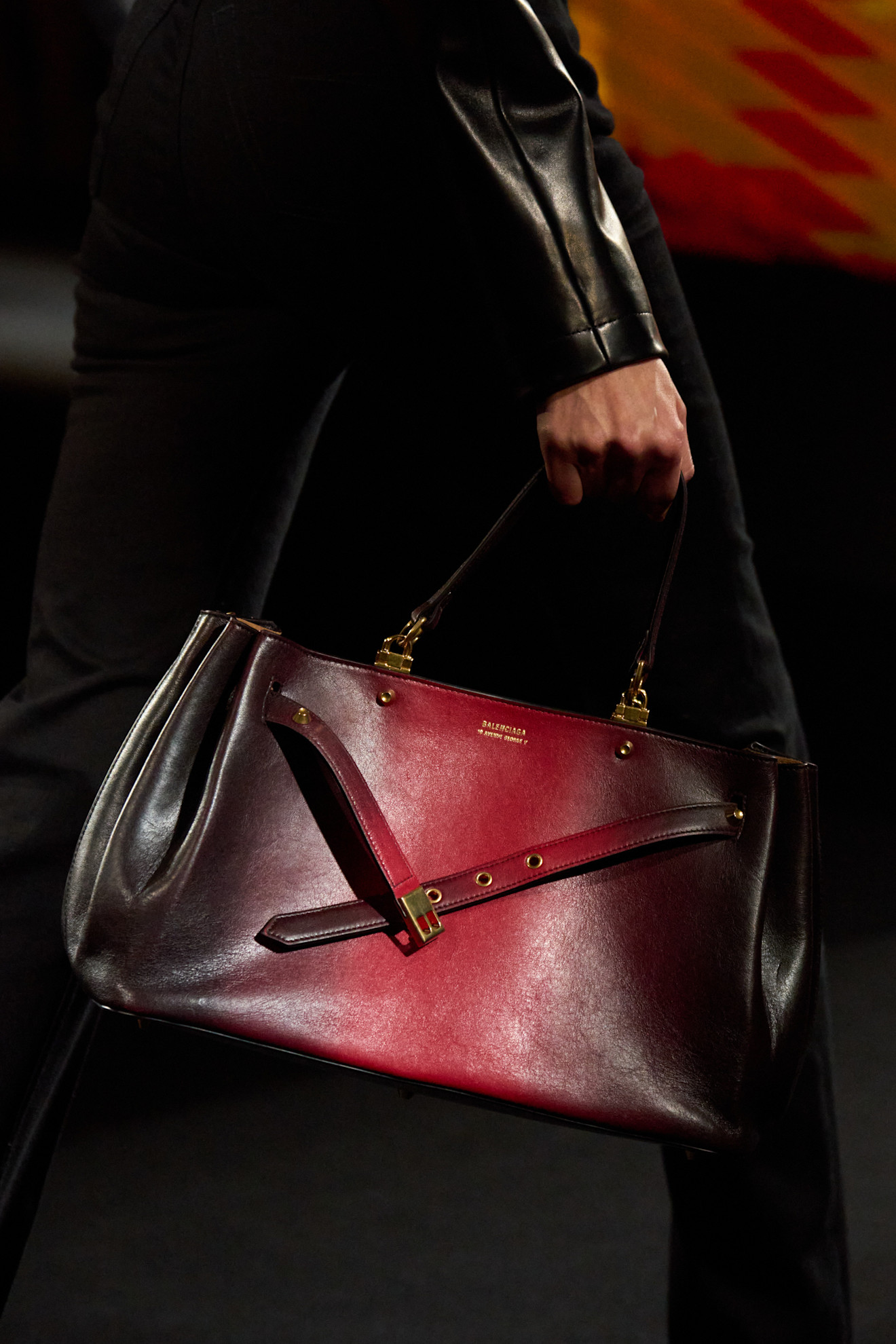A close-up shot of a model walking in the Balenciaga F/W 26 show during Paris Fashion Week carrying an ombr&amp;eacute; red-and-black top-handle bag.