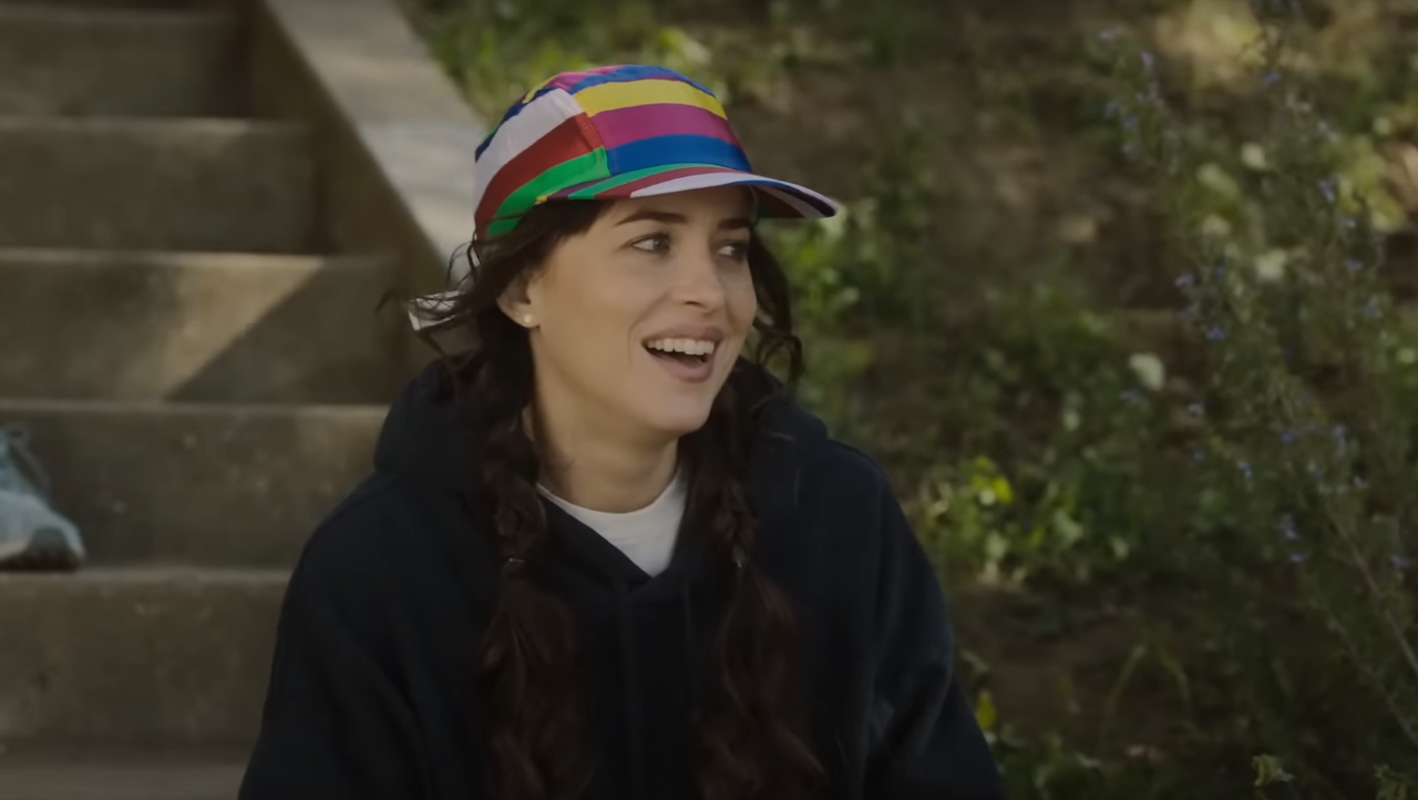 Dakota Johnson smiling in a rainbow hat in Am I OK?