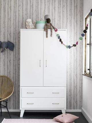 white wardrobe infront of woods wallpaper with bunting in a kid's room