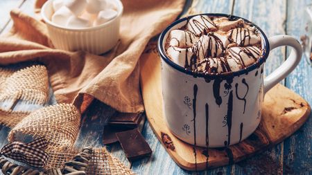 A cup of hot chocolate with marshmallows and chocolate drizzled over the top