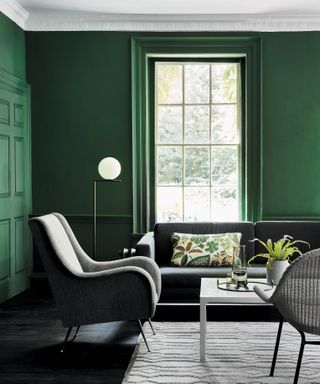 Green living room with gray sofa, armchair and rug, white coffee table, patterned cushion, black floor, floor lamp, designers favorite green paint colors, dark green dining room in Little Greene paint