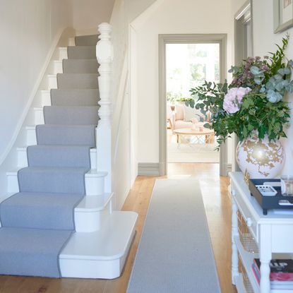 Wooden floor with grey runner next to white stair case with grey stair runner