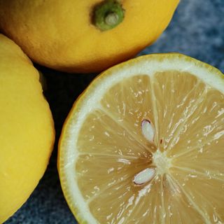 A close-up shot of a cut lemon, alongside two uncut lemons. Seeds are visible.