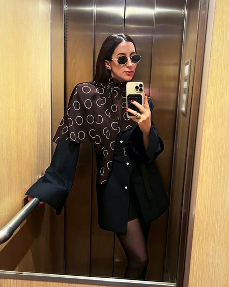 Caitlin Burke wearing a Prada cape and sunglasses in an elevator. 