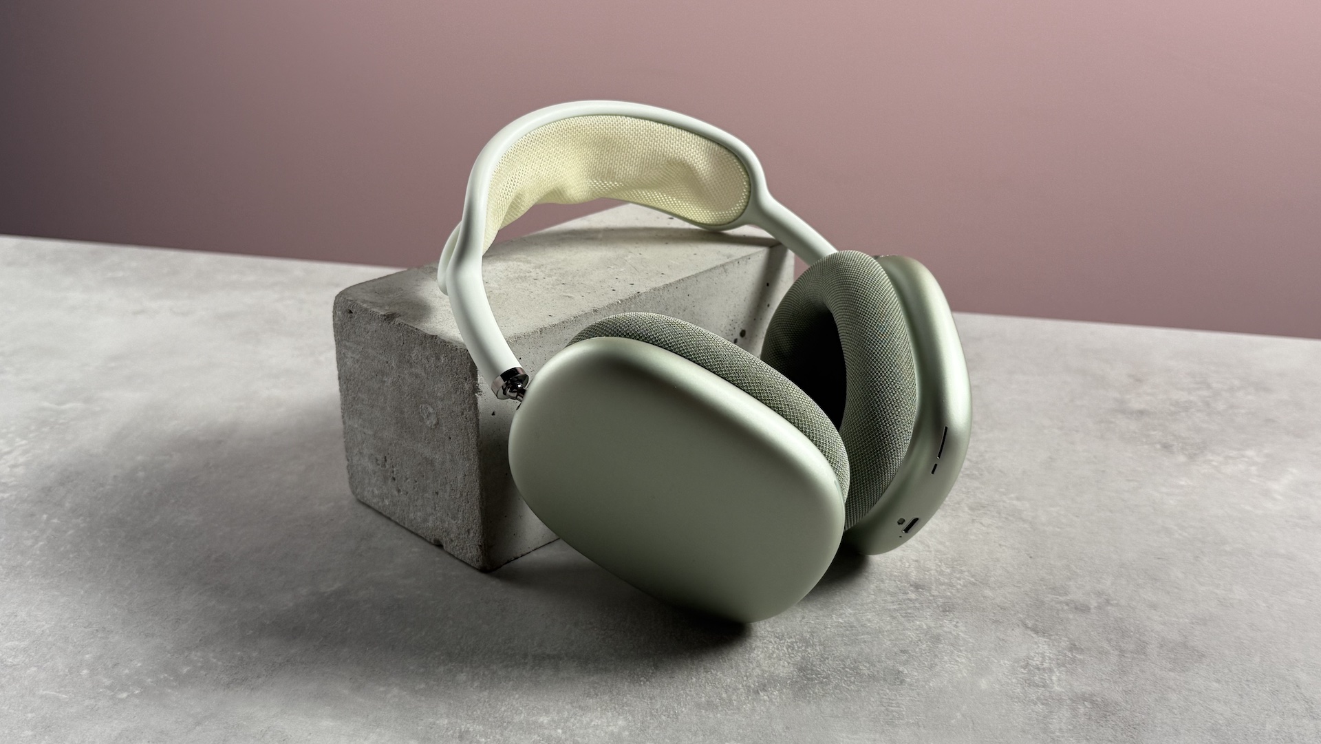 The AirPods Max propped up at a 3/4s angle in front of a pink background.