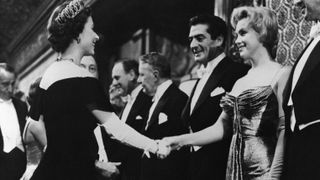 Queen Elizabeth II of England offers a gloved hand to Hollywood star Marilyn Monroe