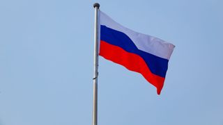 A Russian flag flying on a pole against a blue sky
