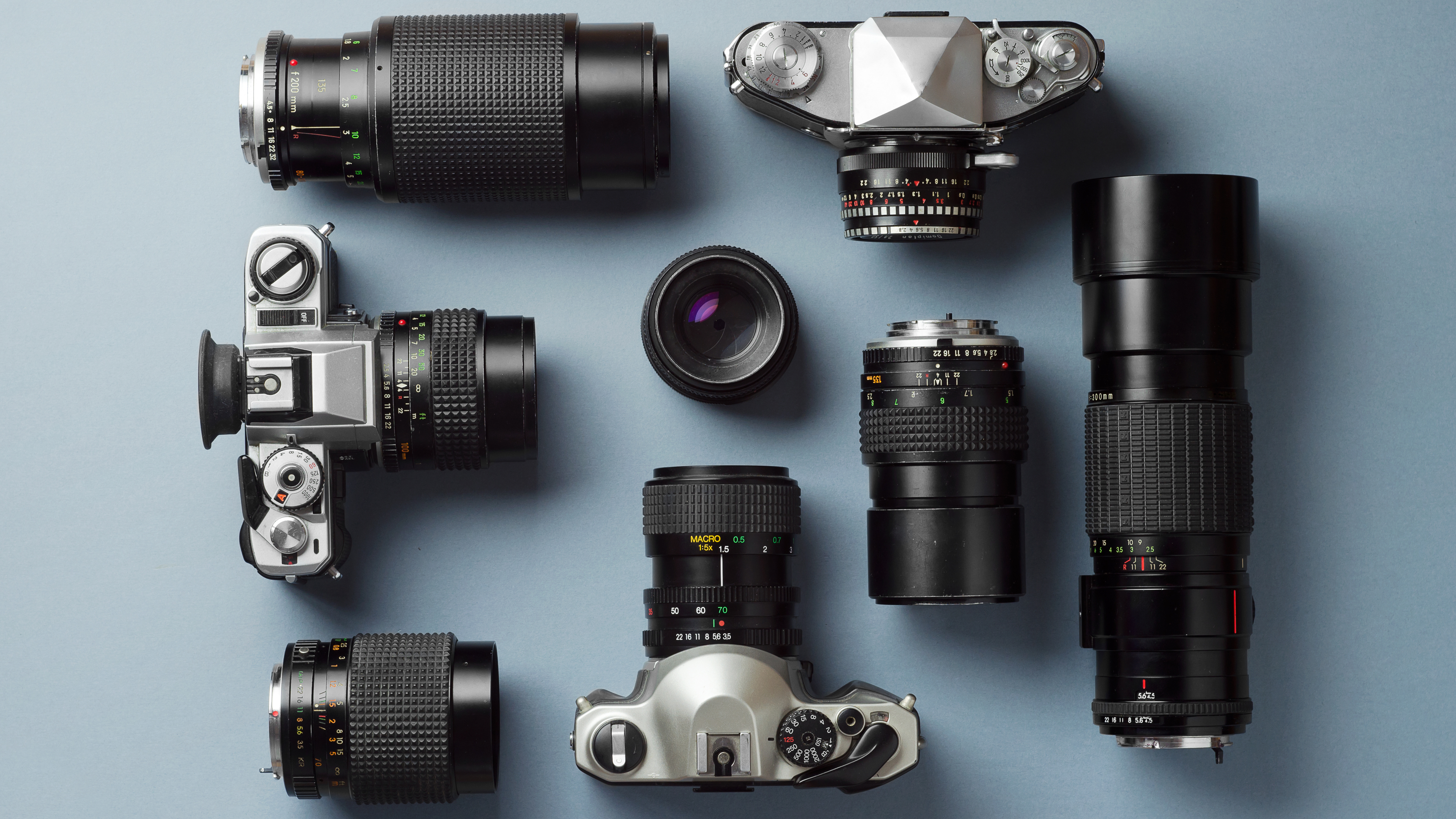 A collection of film cameras and lenses on a blue background