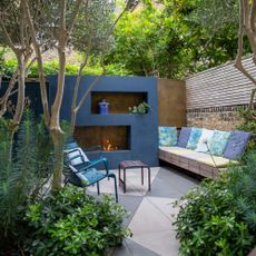 lush mediterranean oasis garden with blue painted wall and fireplace bench seating with cushions