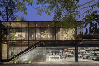 A street level view of the exhibition workshop space from outside at night time. The two storey building is illuminated and looks like a modern shipping container.