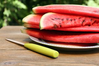 A pile of cut watermelon sits on a picnic table.