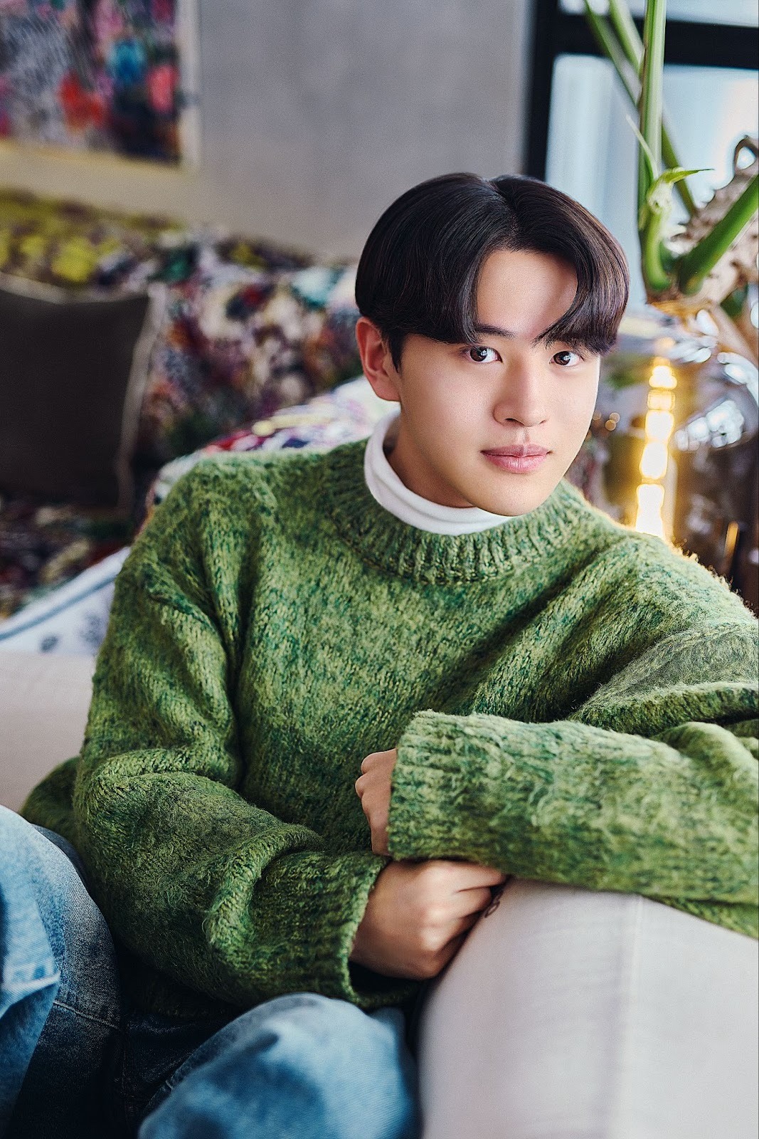 A Japanese man named Ryuki wears a green knitted sweater and jeans while sitting on a sofa, in a cast portrait for 'The Boyfriend.'