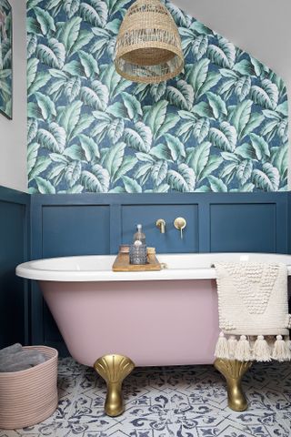 Blue panelled bathroom with palm print patterned wallpaper, patterned floor tiles and pink roll-top freestanding bath